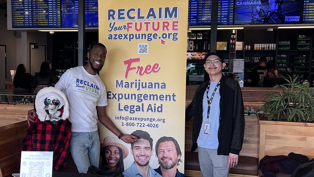 Two people standing in front of a retractable banner that reads Reclaim Your Future: Free Marijuana Expungement Legal Aid
